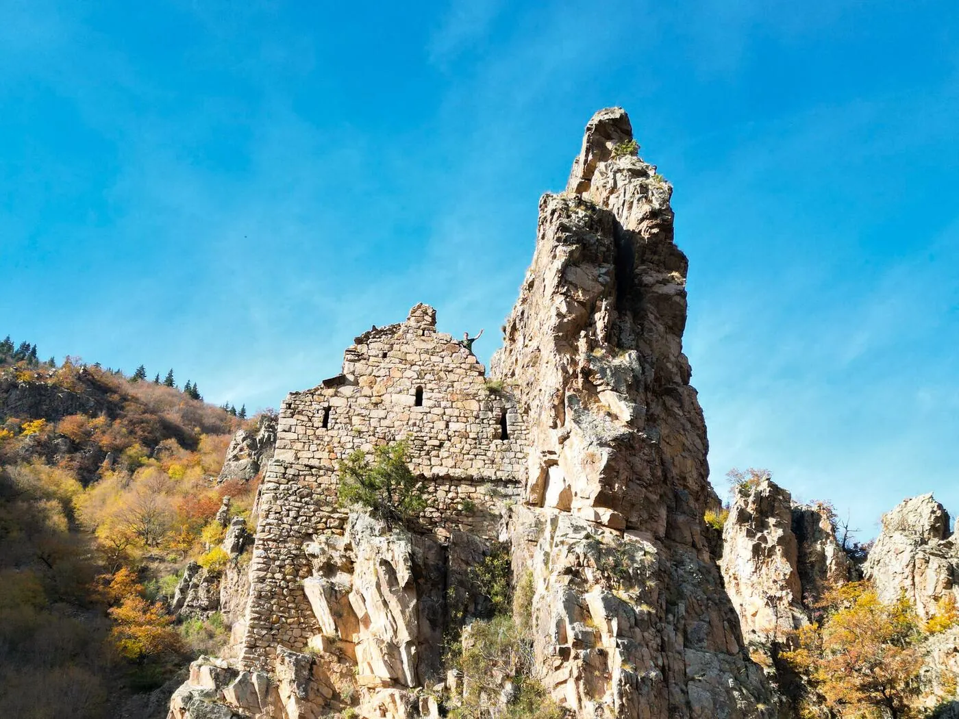 Nuka Sakdari seen from the valley floor, standing on its rock spur against a blue sky, with the autumn slope behind.