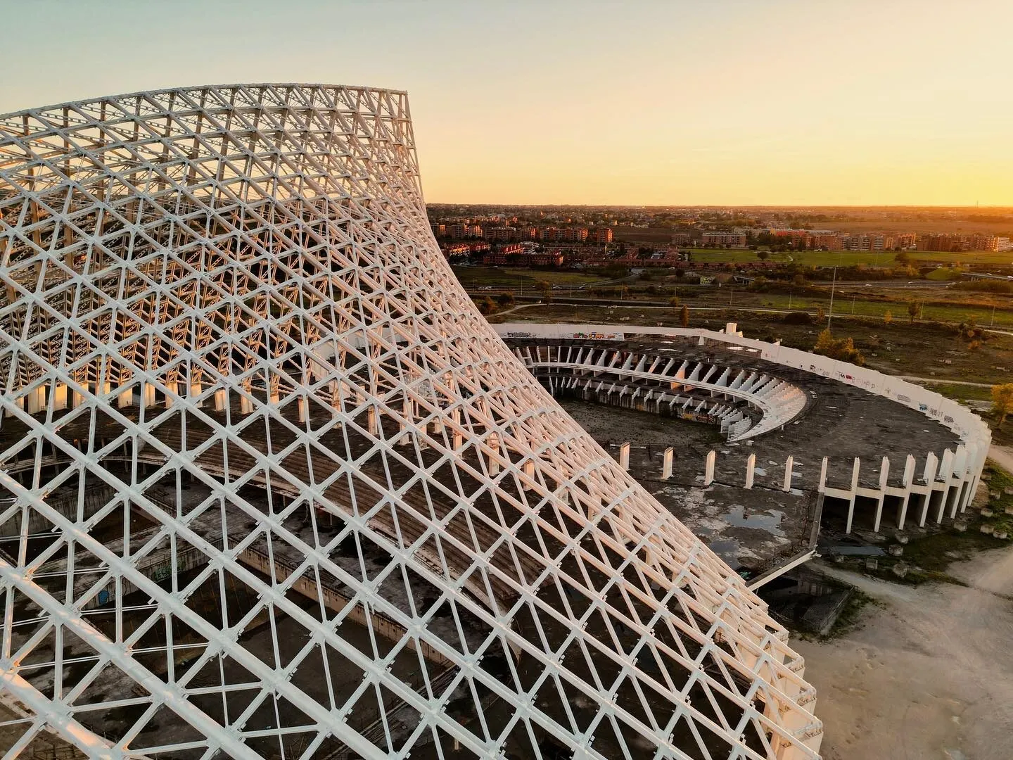 Aerial drone photograph at dusk of La Vela di Calatrava, Santiago Calatrava's vast white steel structure over the unfinished Città dello Sport in Rome, city lights on the horizon