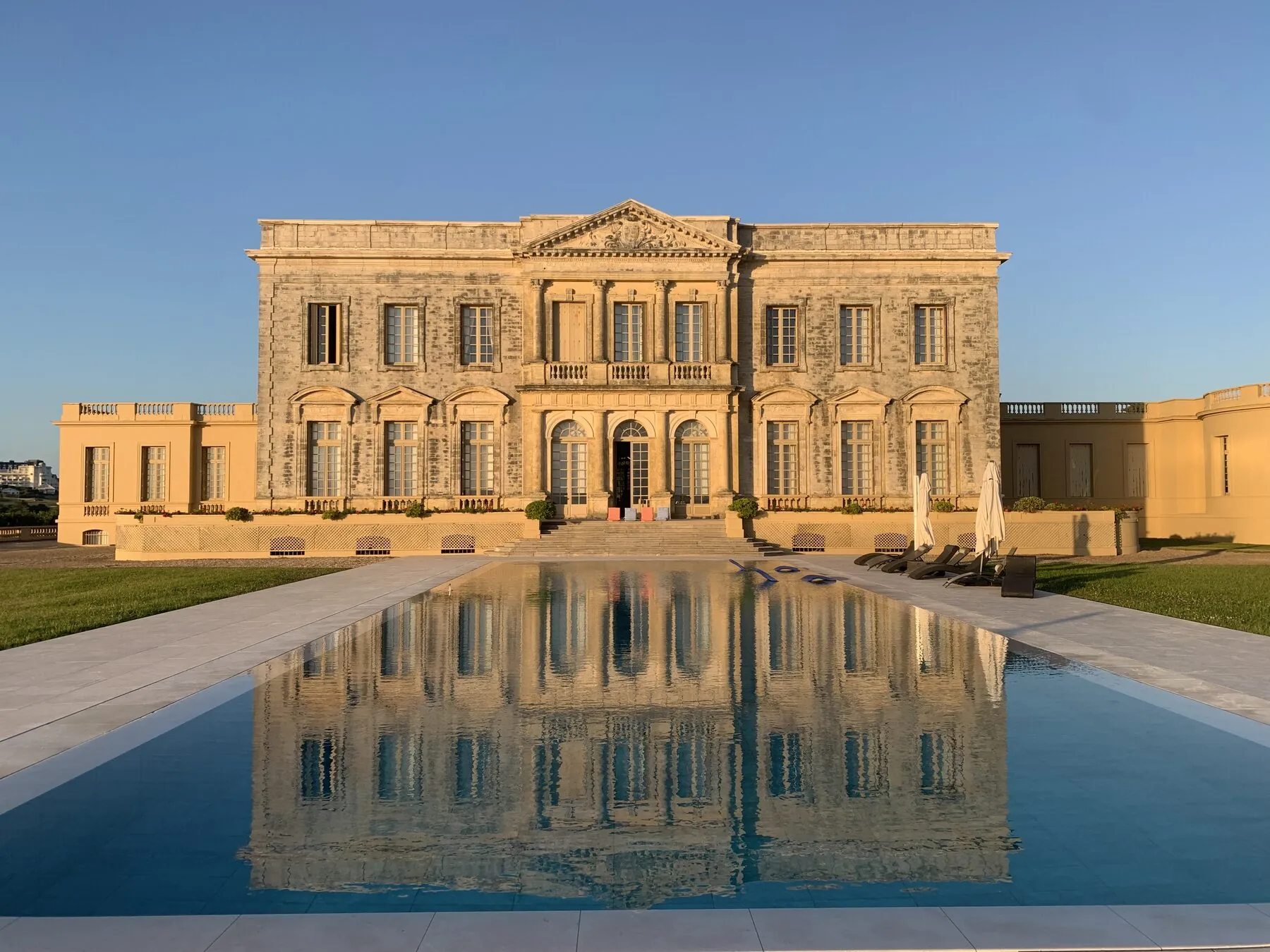 A symmetrical honey-stone neoclassical palace at golden hour, perfectly mirrored in a long, still reflecting pool