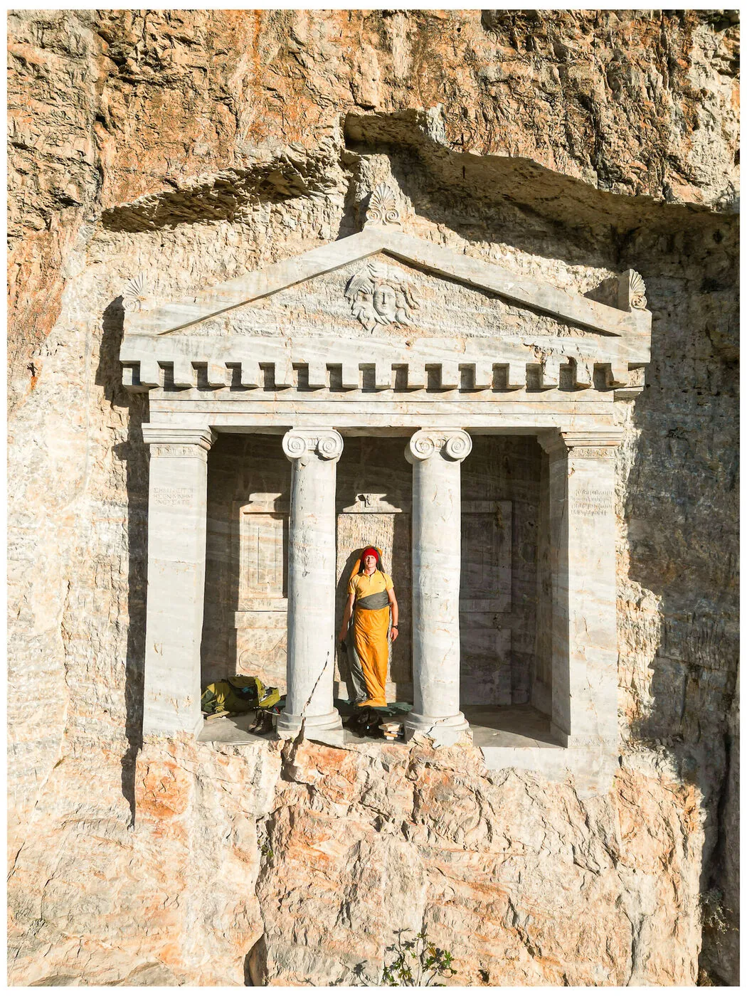 A rock-cut classical tomb facade with a figure in a sleeping bag between the pillars