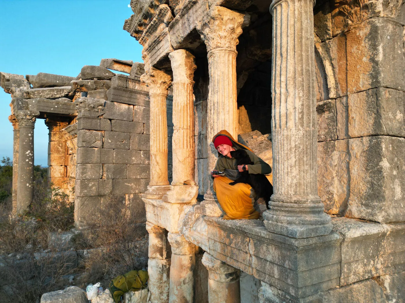 Tassilo with Fluffo, his black dog, among Roman colonnade ruins at sunset
