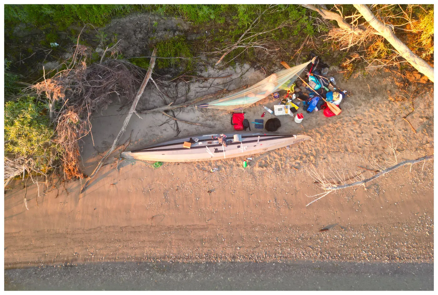 Top-down drone view of a man asleep beside his loaded kayak on the sand