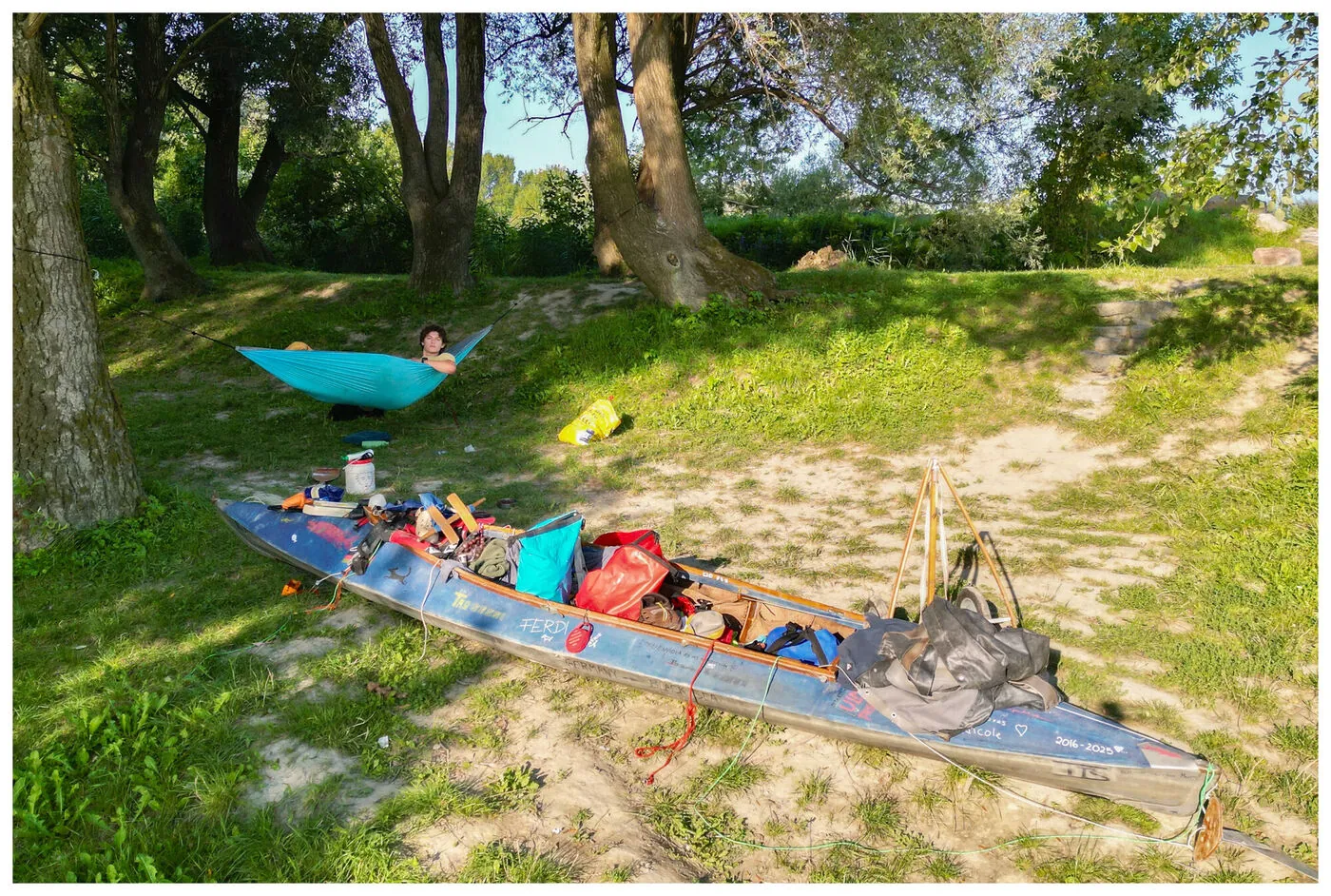 Aerial of a hammock and a blue kayak on a riverbank in warm evening light